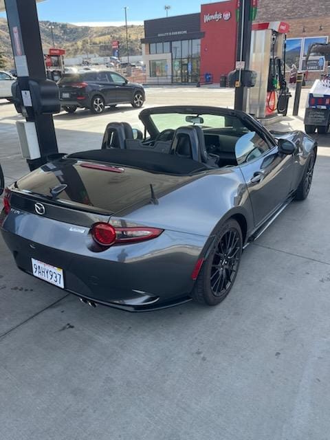 A silver convertible sports car refueling at a gas station.