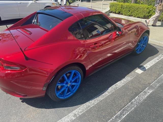 Red sports car with bright blue wheels parked in a lot.