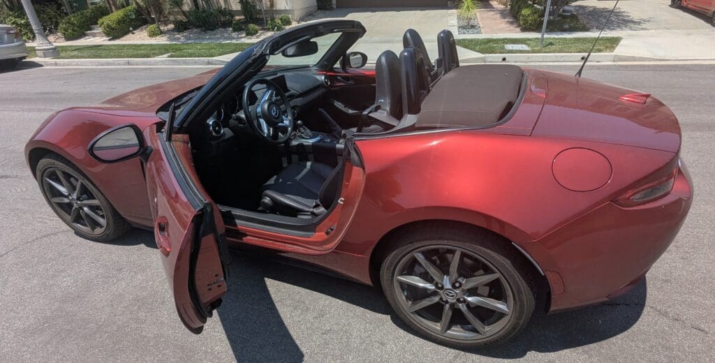 Red convertible sports car with open driver door and black interior.