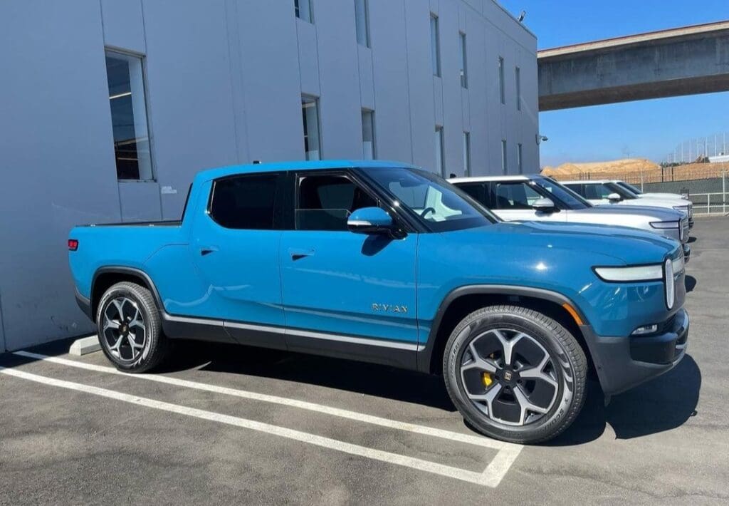 Blue electric pickup truck parked outside a building on a sunny day.