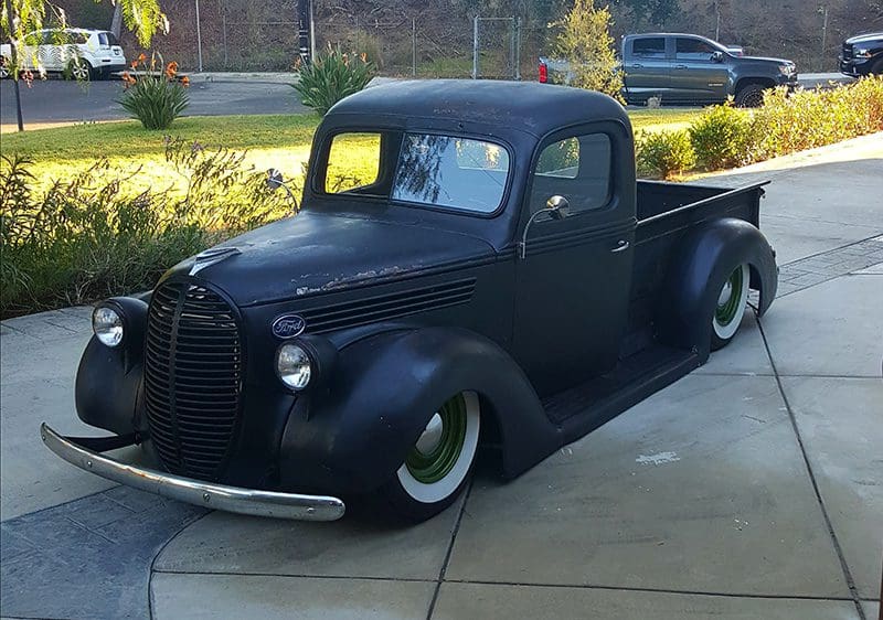 A matte black vintage pickup truck parked on a driveway.