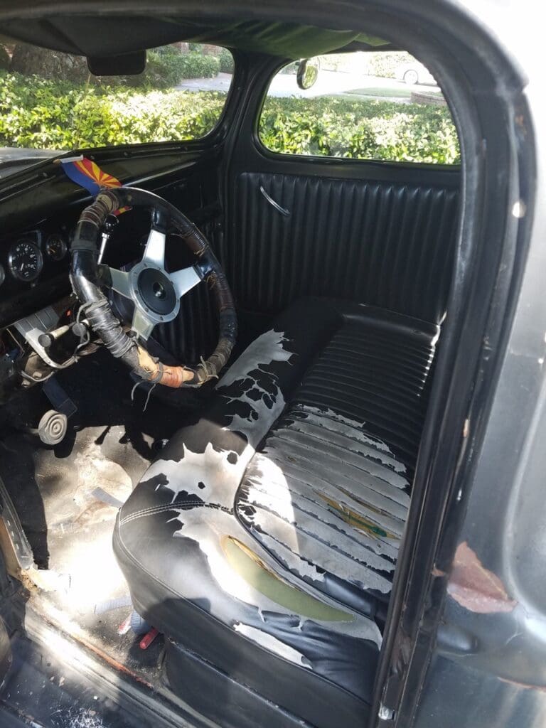 Interior of a worn vintage car showing a damaged seat and steering wheel.