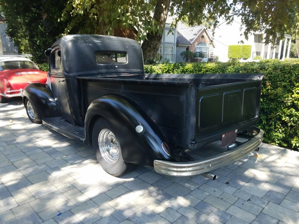 Vintage black pickup truck parked under a tree on a sunny day.