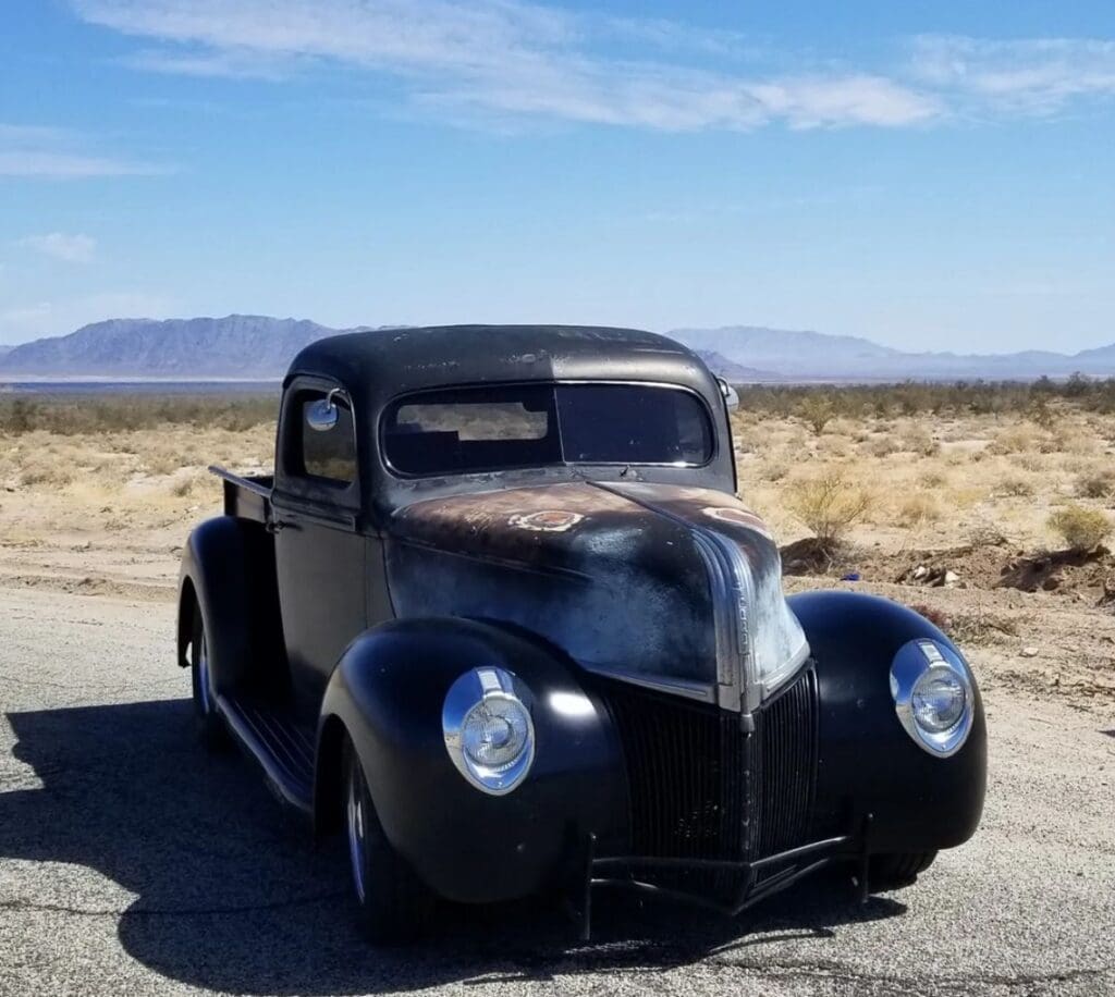 Classic black vintage car parked in a desert landscape under a blue sky.