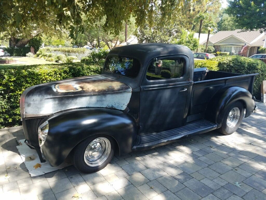 Vintage black pickup truck parked on a sunny driveway.