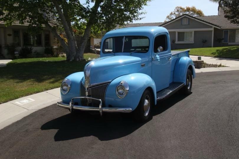 Classic blue vintage pickup truck parked on a sunny suburban street.