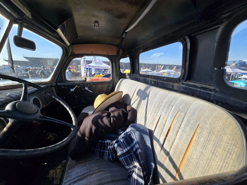 Interior of an old truck with a plaid shirt and other items on the bench seat.