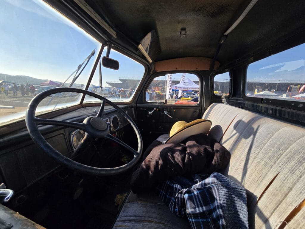 Interior of an old truck cab with a worn steering wheel and a sleeping dog on the seat.