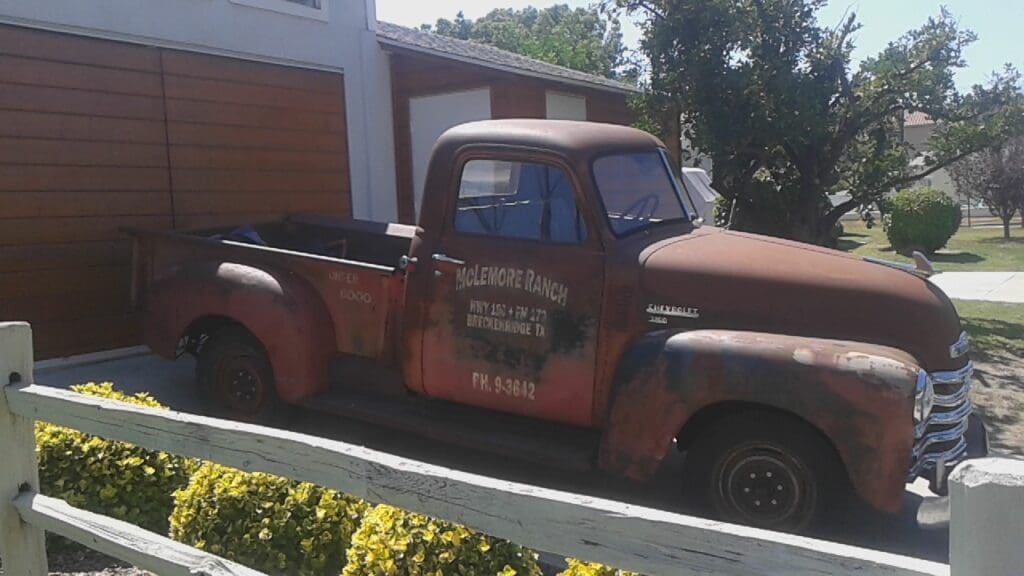 Rusty vintage pickup truck parked near a garden.