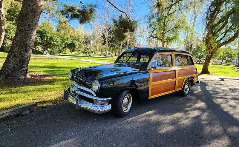 Classic black and wood-paneled vintage car parked in a sunny park.