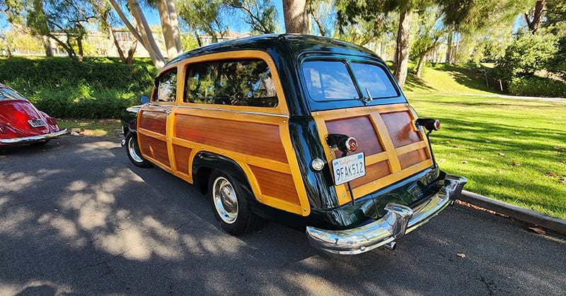Classic woody station wagon parked outdoors under trees.