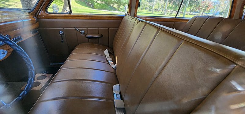 Vintage car interior with brown leather seats and seat belts.