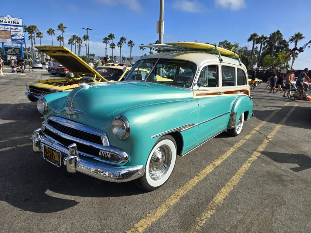 Vintage turquoise and white classic car parked at a sunny outdoor show.