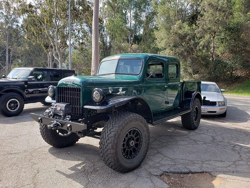 A rugged green off-road pickup truck with large tires in a wooded area.