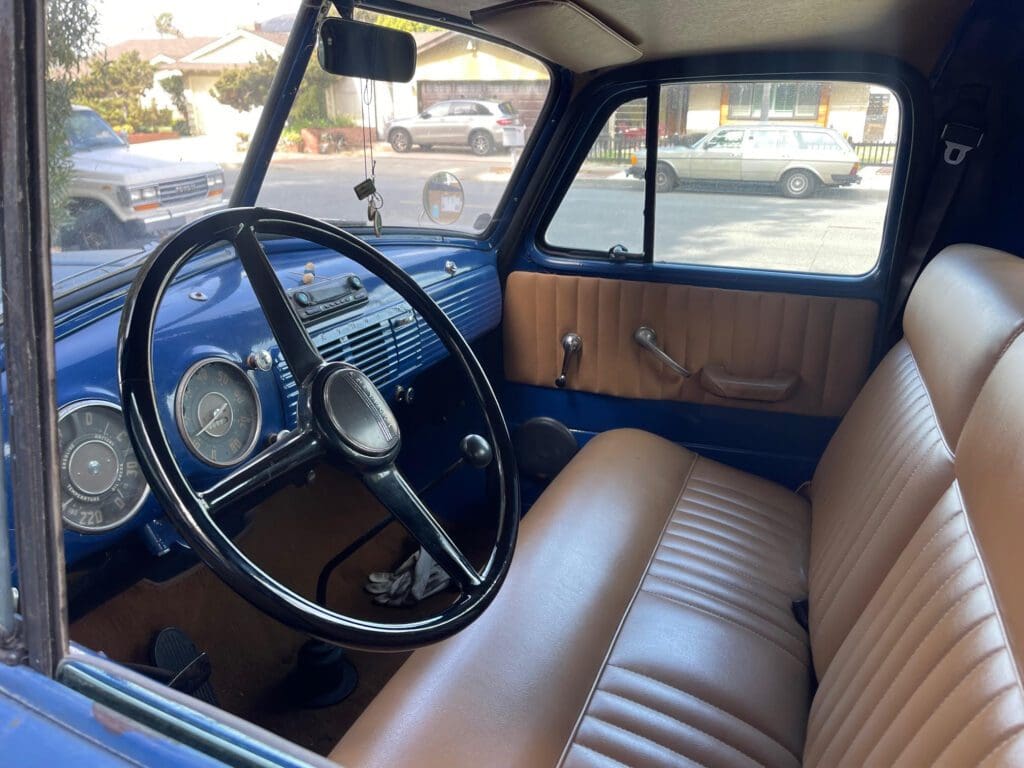 Interior of a vintage car with tan leather seats and a classic steering wheel.