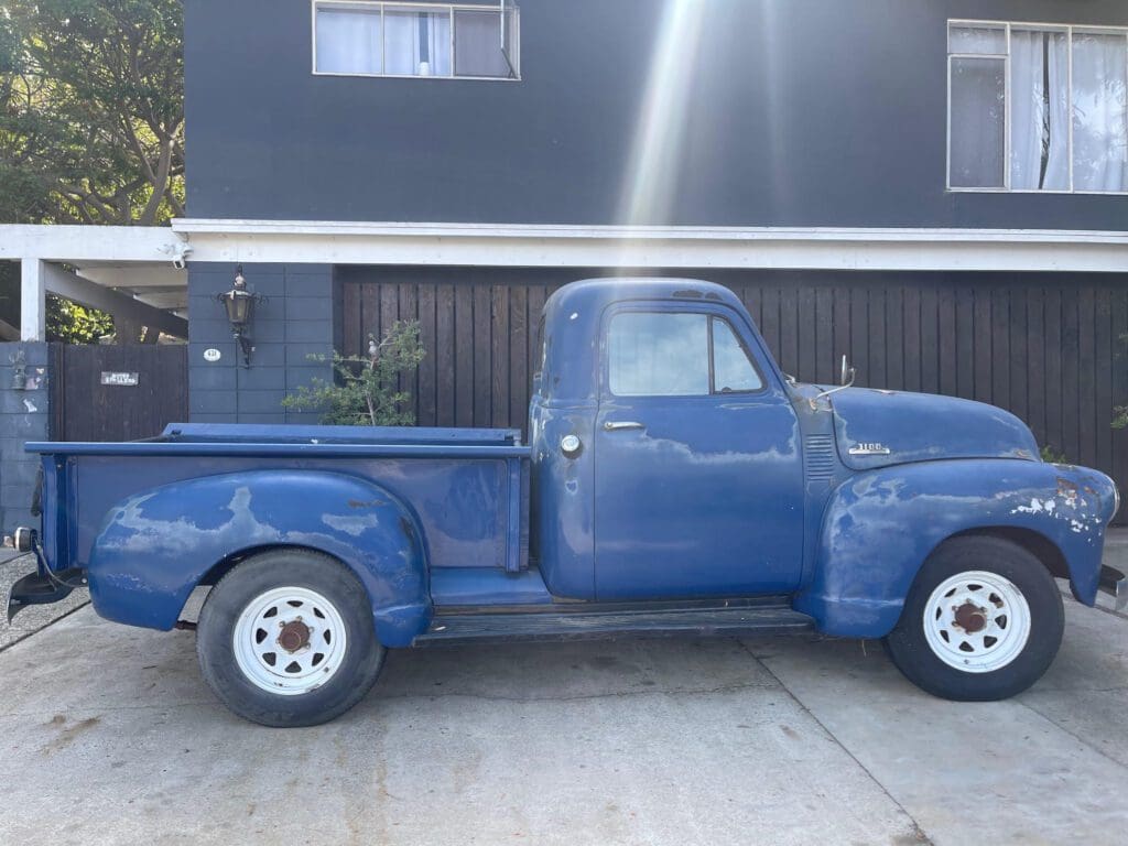 A vintage blue pickup truck parked in front of a modern house.