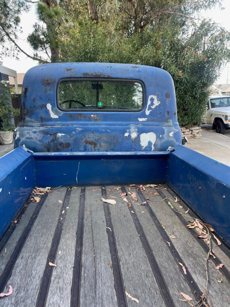 Old blue pickup truck bed with peeling paint and some rust.