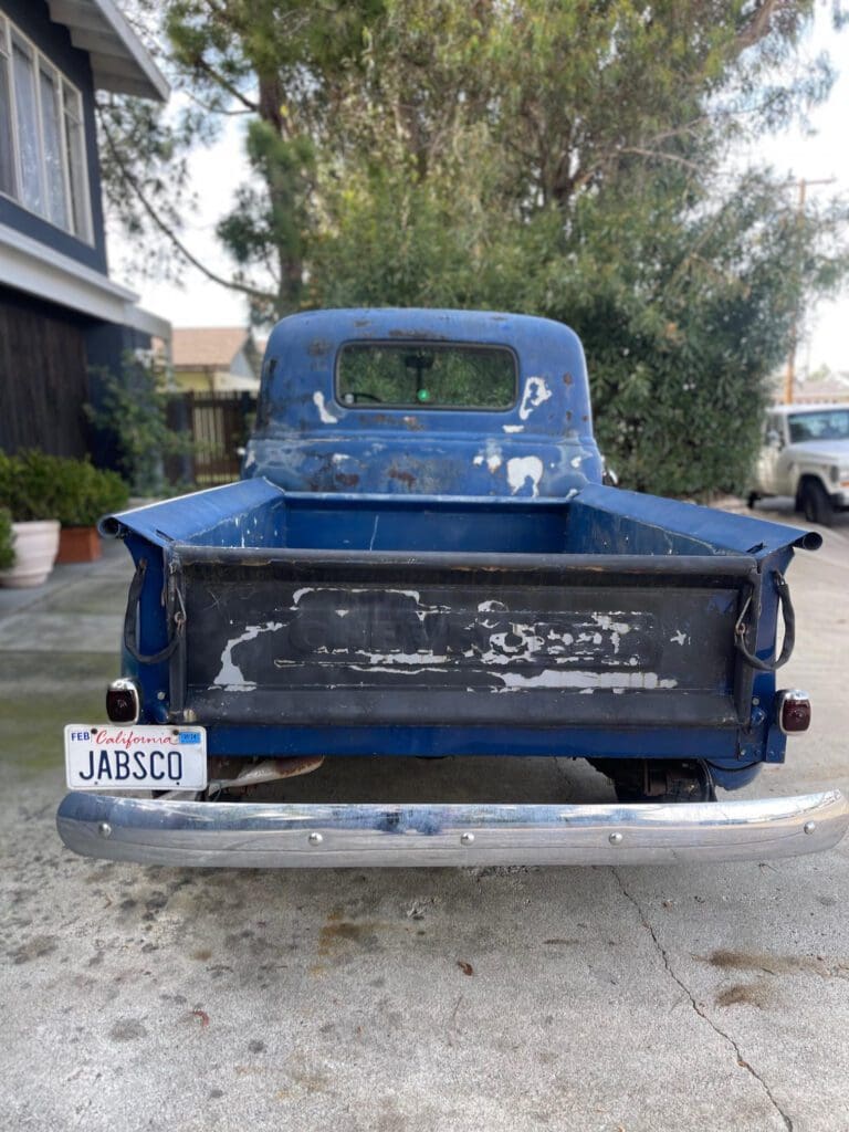 Rear view of a vintage blue pickup truck with a worn tailgate.