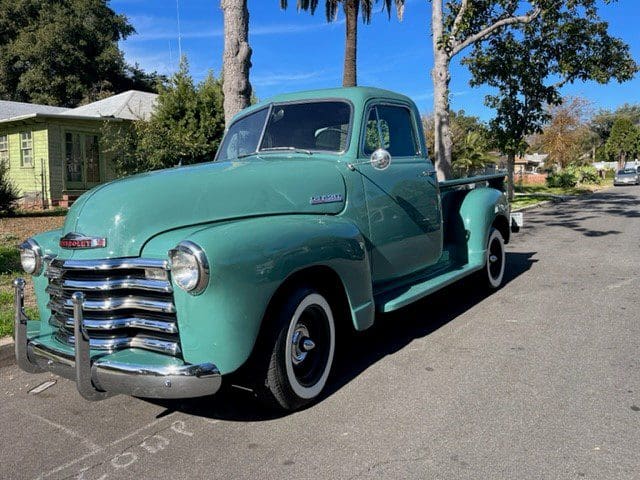 Classic green vintage pickup truck parked outdoors on a sunny day.