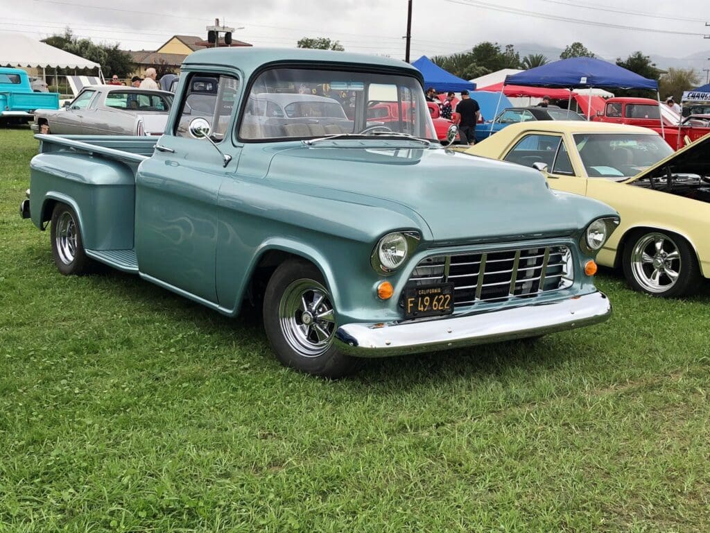 Classic mint green pickup truck parked on grass at a car show.