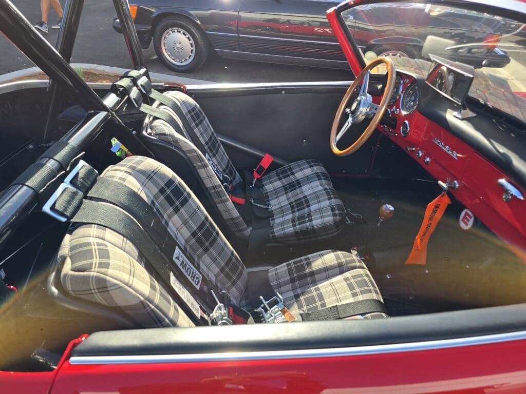 Interior of a vintage convertible with plaid seats and wooden steering wheel.