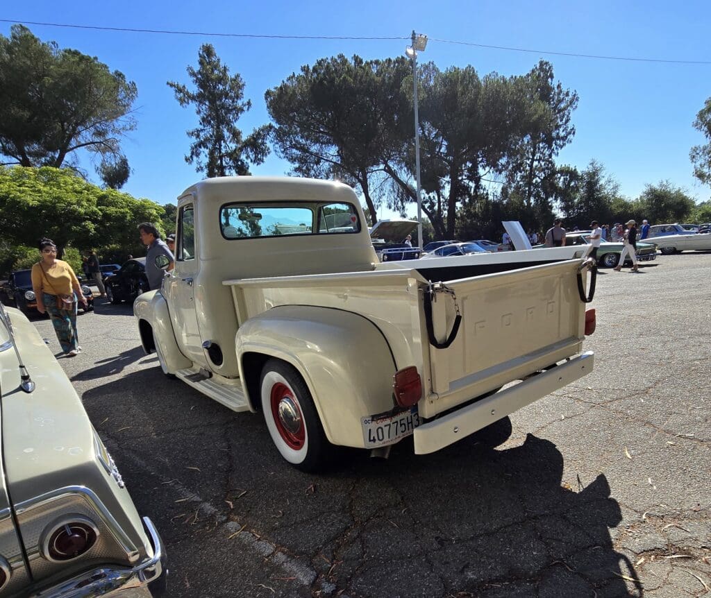 Classic cream vintage pickup truck with red-rimmed whitewall tires parked outdoors.