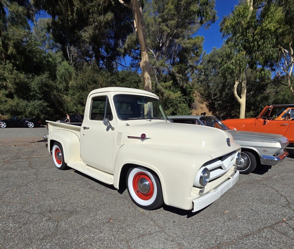 Classic white pickup truck with red rims parked outdoors on a sunny day.