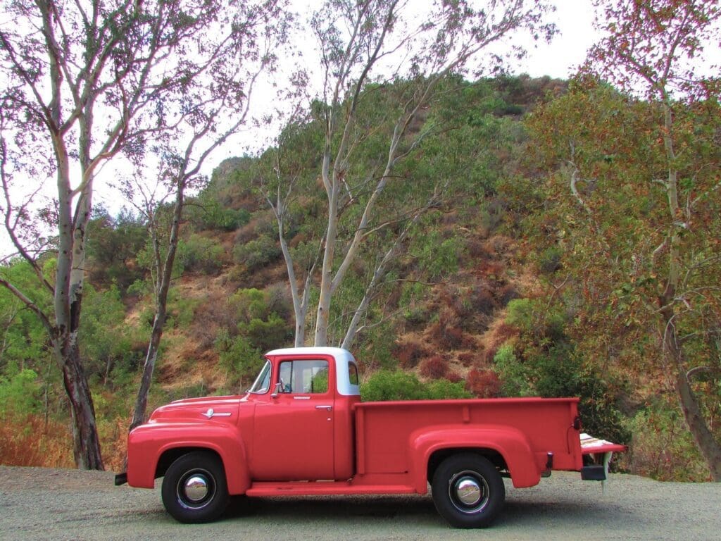 Classic red vintage pickup truck parked by a hillside.