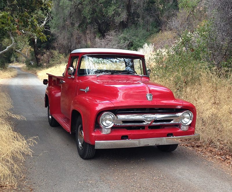 A red vintage pickup truck driving on a rural road.