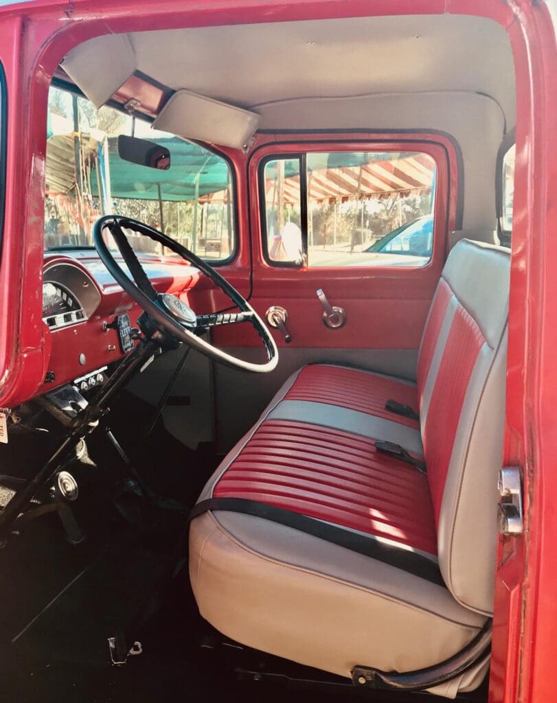 Interior of a vintage red truck with classic dashboard and bench seating.