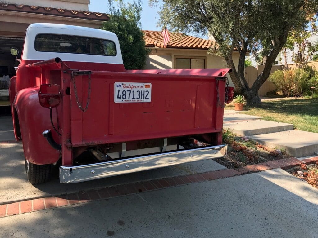 Red dumpster with a California license plate parked on a suburban street.