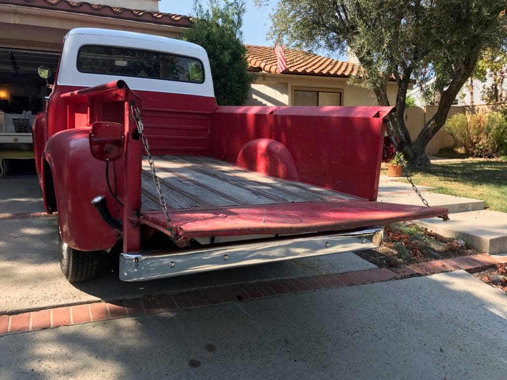 Red vintage pickup truck with tailgate down in a sunny driveway.