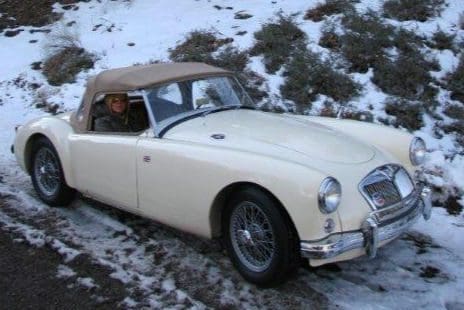 Classic white convertible car parked on snowy ground with two people inside.