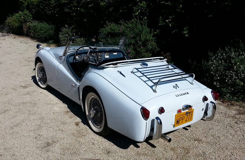 Classic white convertible car parked outdoors in sunlight.
