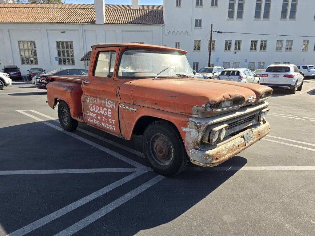 Rusty vintage pickup truck parked in a lot with faded text on the door.
