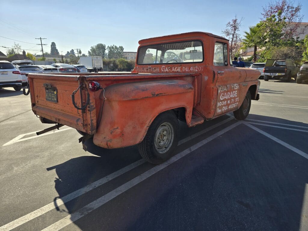 Rusty vintage pickup truck parked in a lot under clear skies.