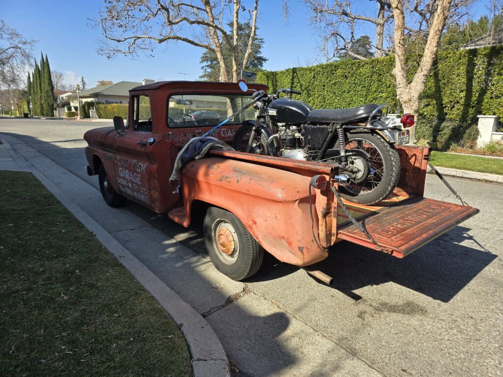Rustic pickup truck carrying a vintage motorcycle in its bed.