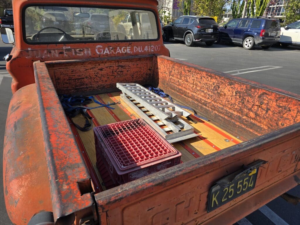 Rusty red pickup truck bed with wooden planks and a radiator.
