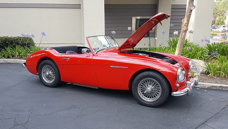Classic red convertible vintage car with hood open in a driveway.