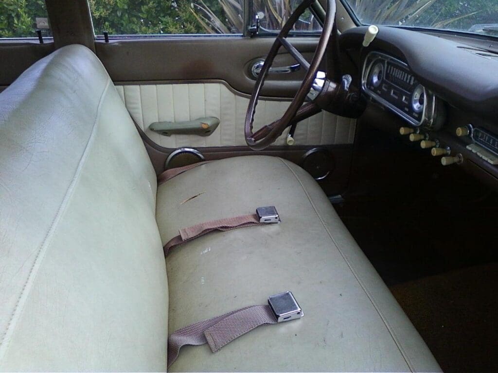 Vintage car interior with bench seat and classic steering wheel.