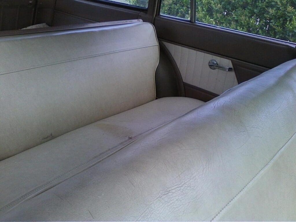 Inside view of an old car with beige fabric bench seats.