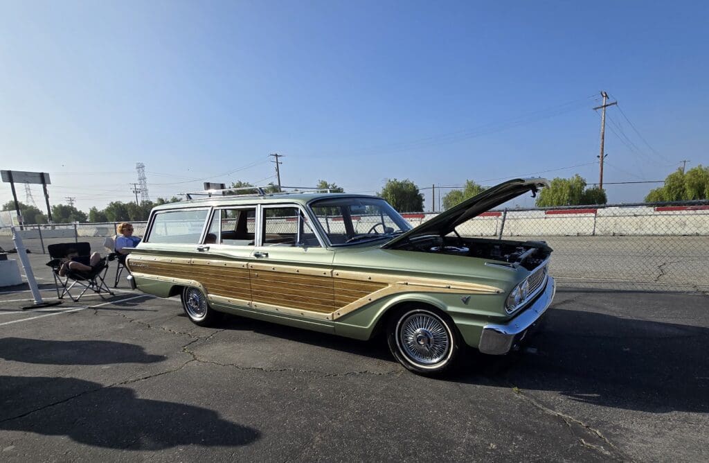 Classic vintage station wagon with wood paneling and hood open under clear sky.