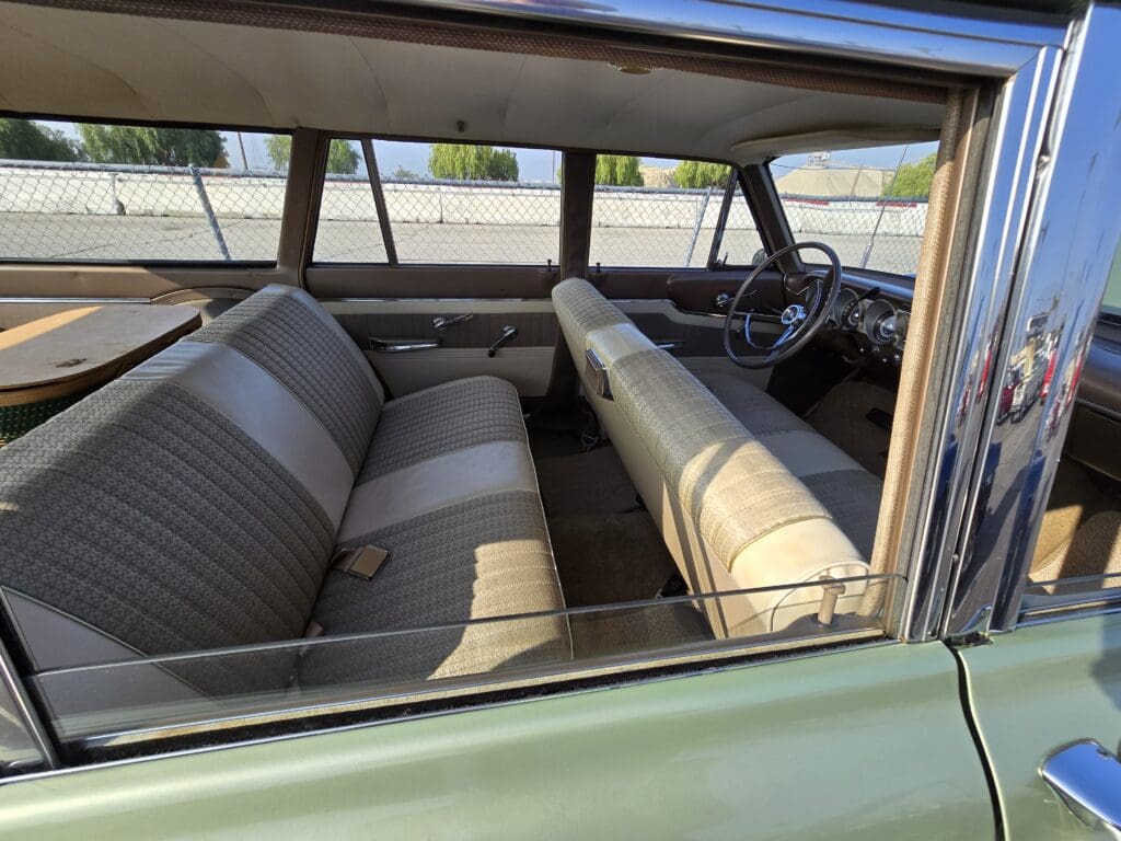 Interior of a vintage car with beige bench seats and large windows.