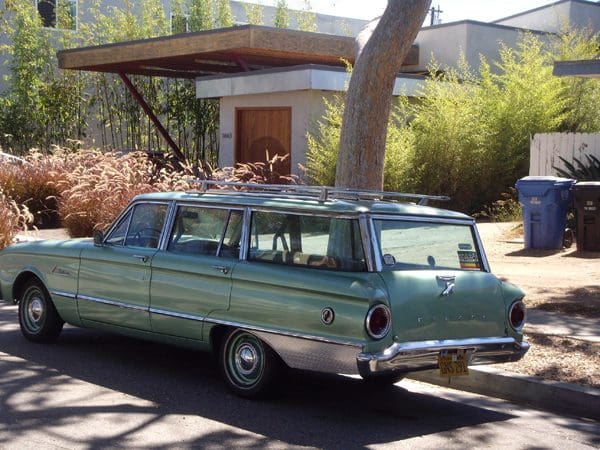 Vintage green station wagon parked near a mid-century modern house.