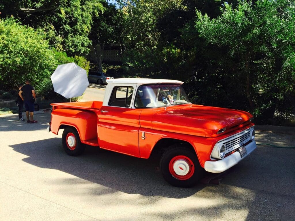 Bright orange vintage truck parked on a sunny driveway.