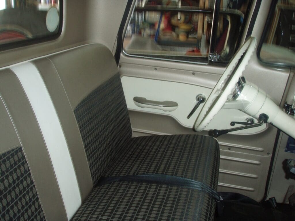 Classic car interior with vintage bench seats and steering wheel.