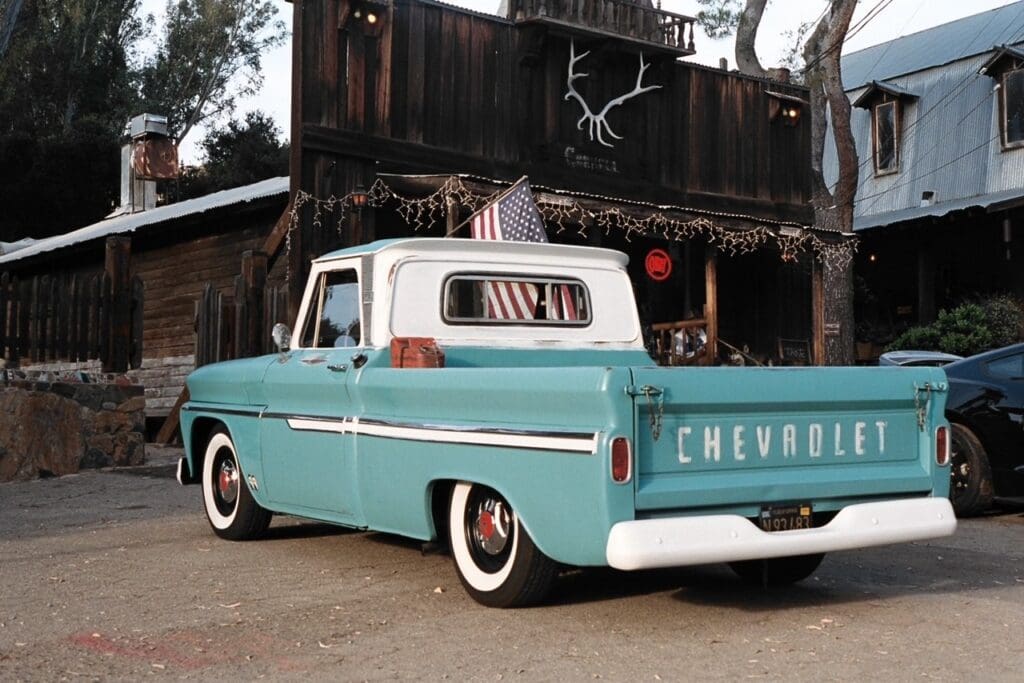 Classic teal Chevrolet pickup truck parked near rustic wooden building with antlers.