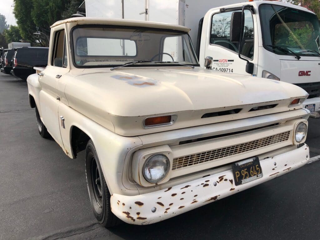 Classic white vintage pickup truck with rust spots parked outdoors.