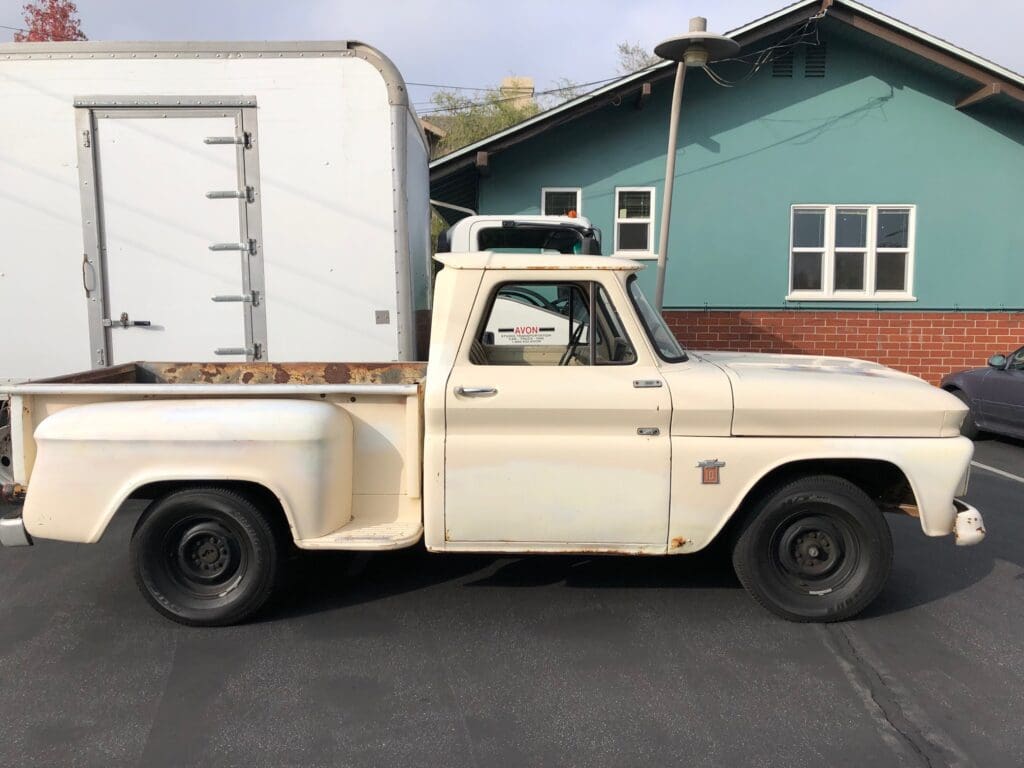Vintage cream-colored pickup truck with a white camper shell parked on a street.