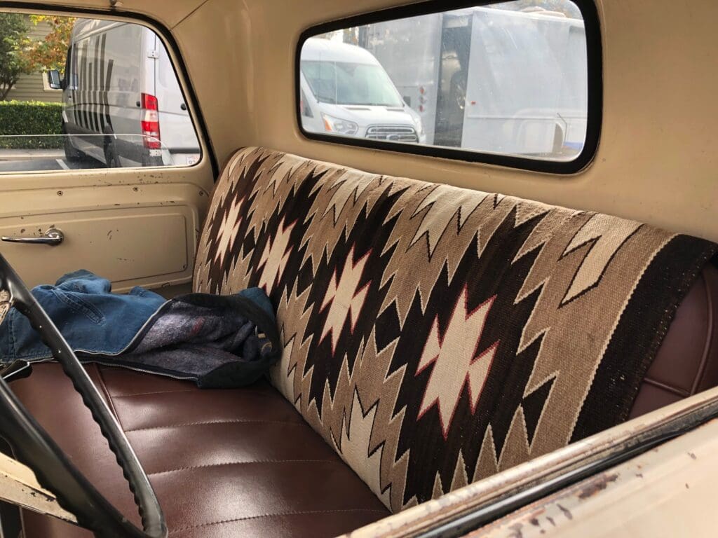 Vintage car interior with patterned seat cover and leather upholstery.